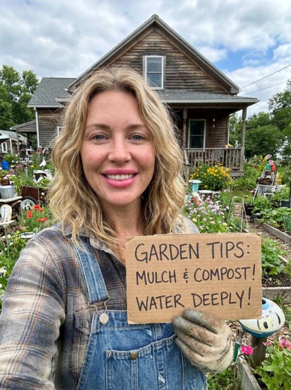 Emily holding a garden tips sign in front of her garden